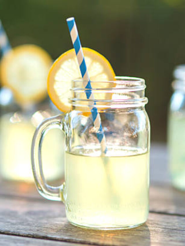 Lemonade glass jars with lemon wedges and straws sitting on a wood tabletop